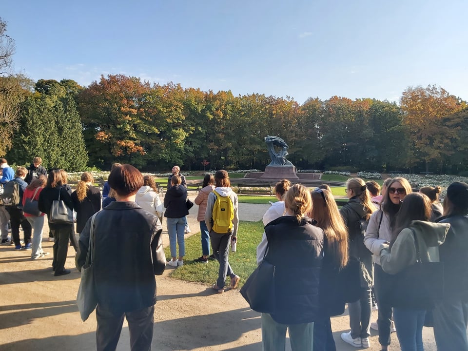 Zespoł pałacowo – parkowy w Łazienkach, uczniowie słuchają przewodnika pod pomnikiem Szopena