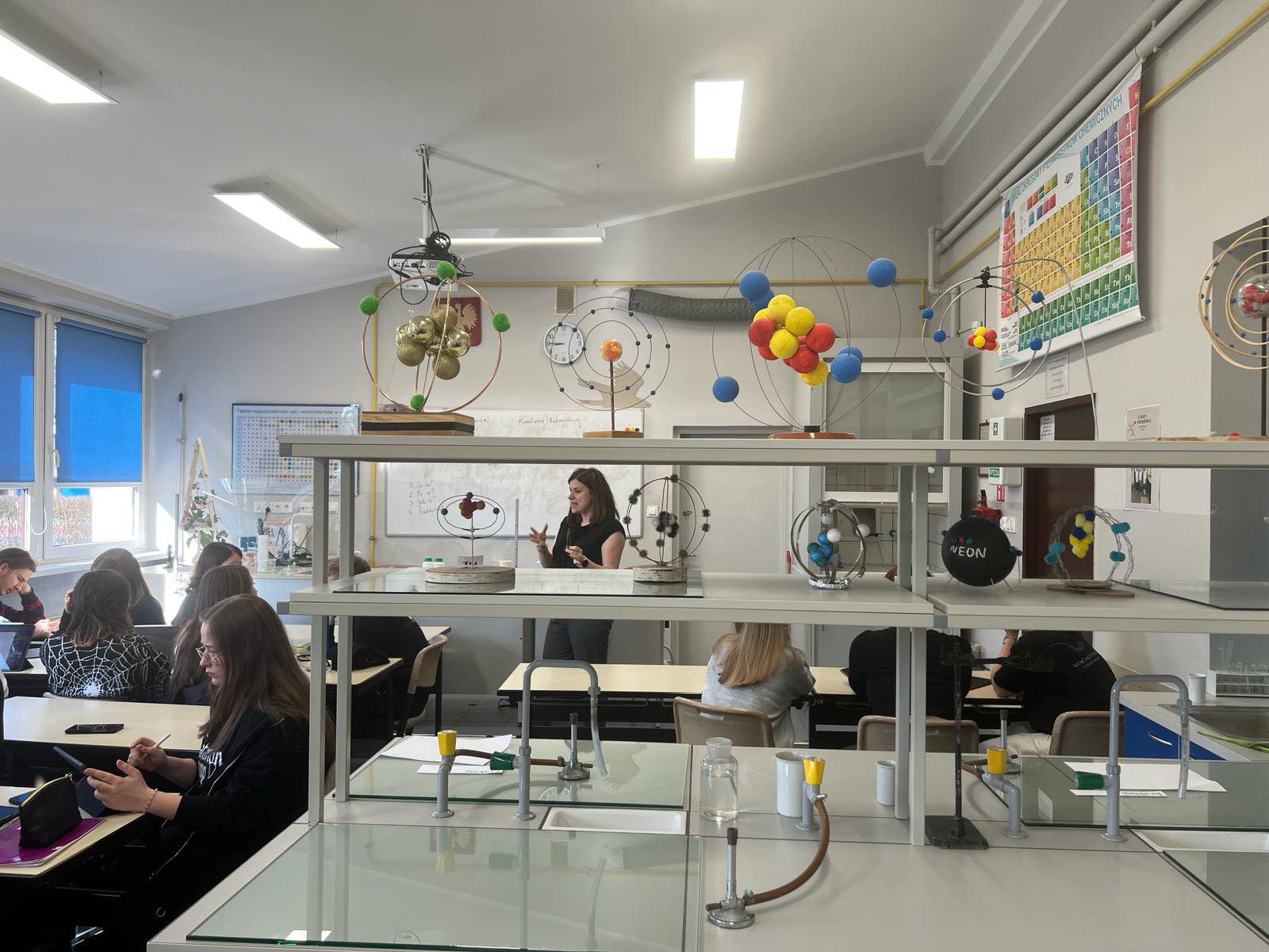 Na zdjęciu uczniowie klasy 2m, podczas zajęć chemicznych, przygotowują doświadczenia, w tle nauczyciel chemii